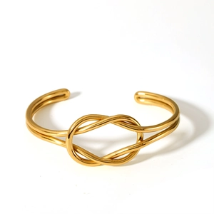 Top-down view of a minimalist 18K gold-plated knotted cuff bracelet on white background