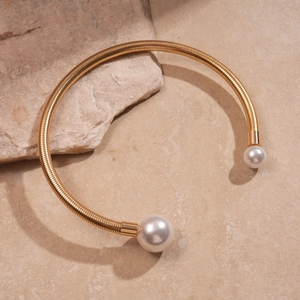 Detail of gold metal torque collar featuring faux pearls on natural stone background