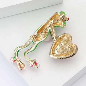 Detail of alloy frog brooch with green enamel finish holding a gold textured heart