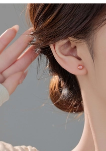 Close-up of a woman wearing a round orange-red gemstone stud earring in a four-prong setting