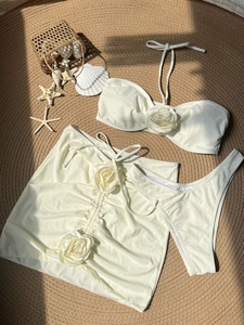 Three-piece cream bikini set with 3D rose flower accents and drawstring skirt on beach mat