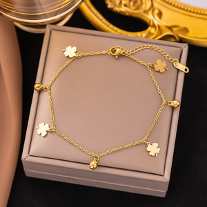 Close-up of gold clover pendants and small beads on a titanium steel anklet over a jewelry box