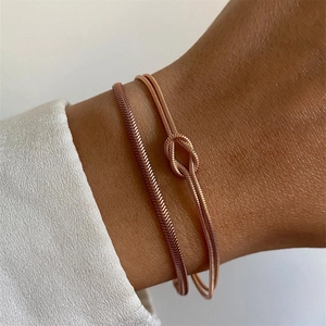 Macro shot of rose gold layered knot bracelet with snake chain texture on woman's wrist