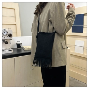 Detail of a large black fringe tote bag worn over the shoulder with a beige suit