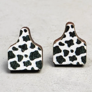 Close-up of wooden cow tag earrings featuring a classic black and white cow print pattern