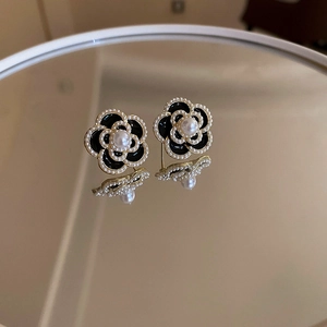 Detail view of French camellia earrings with black enamel and white pearls on gold base