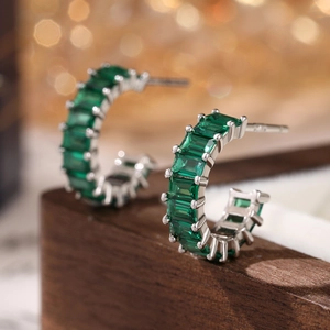 Macro shot of S925 silver C-shaped earrings with emerald-cut green cubic zirconia