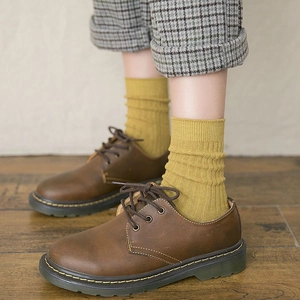 Detail of yellow ribbed crew socks paired with brown leather shoes and yellow stitching