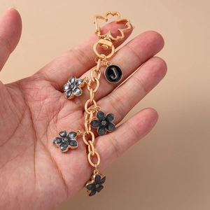 Close-up of gold chain keychain with dark grey enamel flowers and a black letter J pendant