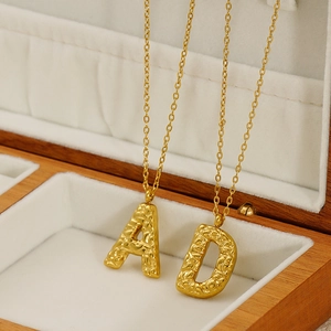Close-up of gold stainless steel A and D letter pendants with embossed textured finish