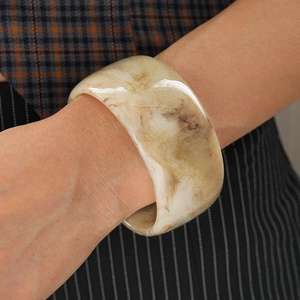 Close-up of a wide marbled resin bangle with amber and white swirling patterns