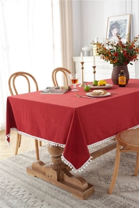 Close-up of red washed cotton tablecloth featuring decorative white pompom fringe details