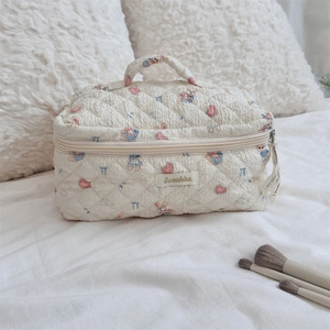 Quilted beige cosmetic bag with cartoon bear pattern and handle on a cozy bed setup
