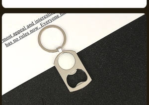 Close-up of a silver metal beer bottle opener keychain with a white golf ball textured inlay