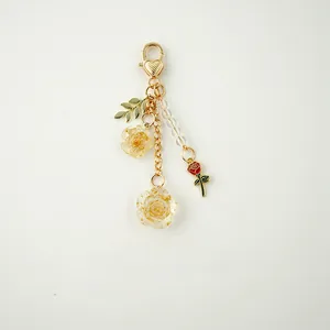 Detail of golden rose keychain with resin flowers and red enamel charm on ivory backdrop