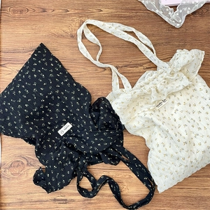 Close-up of floral chiffon tote bags with brand label and long straps on wood background