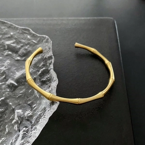 Detail view of a matte gold bamboo-style open cuff bracelet on a black textured surface