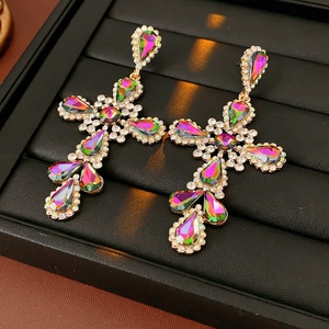 Macro detail of vintage gold cross earrings with iridescent crystals on black leather