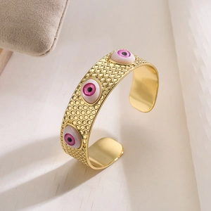 Detail eines 18K vergoldeten Armreifs mit rosa bösen Augen und kreisförmiger Textur