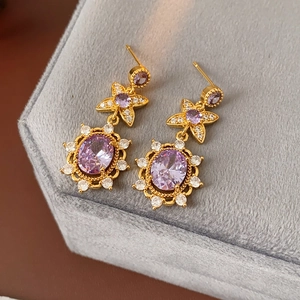 Detail of vintage gold earrings with purple oval gems on gray velvet jewelry box