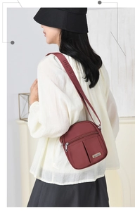 Detailed view of burgundy nylon crossbody bag with dual front zippers worn by a model