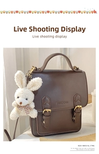 Close-up of a white plush bunny charm with checkered bow on a dark brown leather bag
