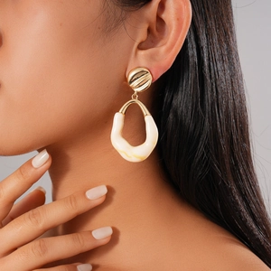 Close-up of golden metal and cream resin geometric earring on a model's ear