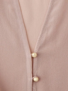 Dettaglio dello scollo a V di una camicetta in raso rosa con bottone dorato rotondo