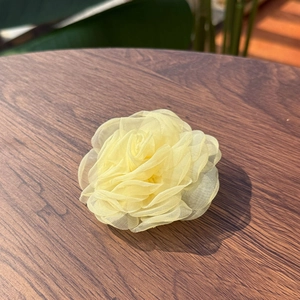 Handmade yellow organza flower hair clip on a wooden surface with a soft natural background