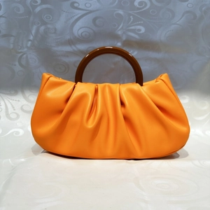 Detailed view of orange ruched cloud bag featuring a large brown resin circular handle