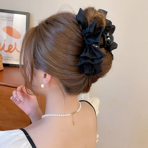 Detail view of a large black ruffled fabric hair claw clip styled on a woman's hair