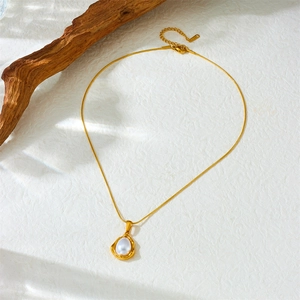 Elegant gold chain necklace with irregular white pearl pendant on a neutral textured background