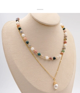 Detail of layered autumn beaded necklace with golden chain and pearl pendant on a stand