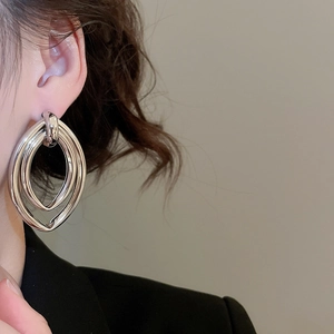 Close-up of a model wearing layered silver geometric oval hoop earrings in minimalist style