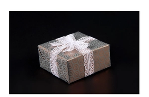 Detail of grey gift box with orange hexagon patterns and white lace ribbon bow