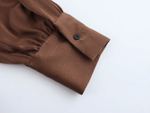 Detail of brown chiffon dress sleeve with smooth satin texture and black button closure