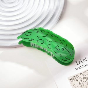 Close-up of a creative cucumber-shaped green hair claw clip on a white textured stone base