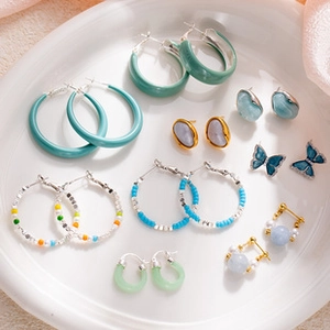 Macro shot of assorted colorful enamel hoop earrings and pearl studs on a ceramic tray