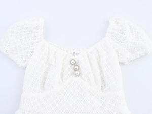 Detail of white lace dress showing pearl buttons, puff sleeves and delicate mesh texture