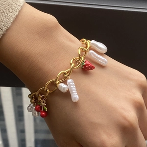 Close-up of gold chain bracelet with pearls, strawberry and cherry fruit charms