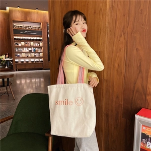Detail of white canvas tote bag featuring pink smile embroidery and lace trim strap
