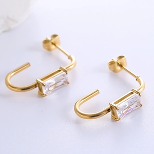 Detail of gold U-shaped earrings with rectangular clear crystal settings on white background