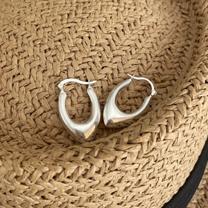 Polished silver U-shaped hoop earrings on a woven straw background for summer vibes