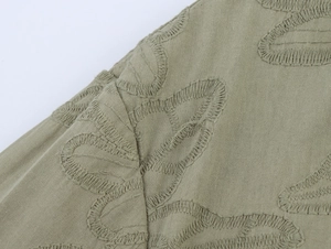 Close-up of sage green blazer fabric featuring intricate floral leaf embroidery details