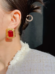 Detail of vintage gold-tone earrings with a large emerald-cut red gemstone on model