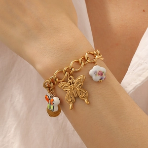 Close-up of a gold chunky charm bracelet with butterfly and floral pendants on wrist