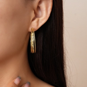 Close-up of golden multi-layer geometric rhombus textured hoop earrings worn by a model
