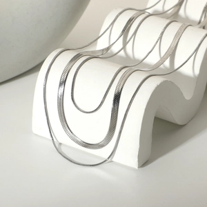 Detailed close-up of layered silver snake chains on a wave-shaped jewelry display stand
