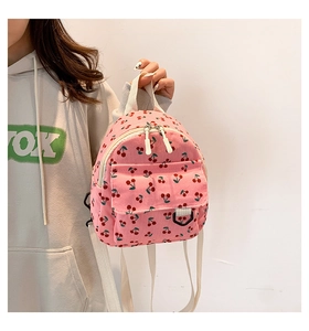 Close-up of pink corduroy mini backpack featuring red cherry patterns and zip detail