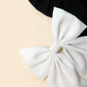 Detailed view of a white satin bow hairclip with flowing tails on a dual-tone background